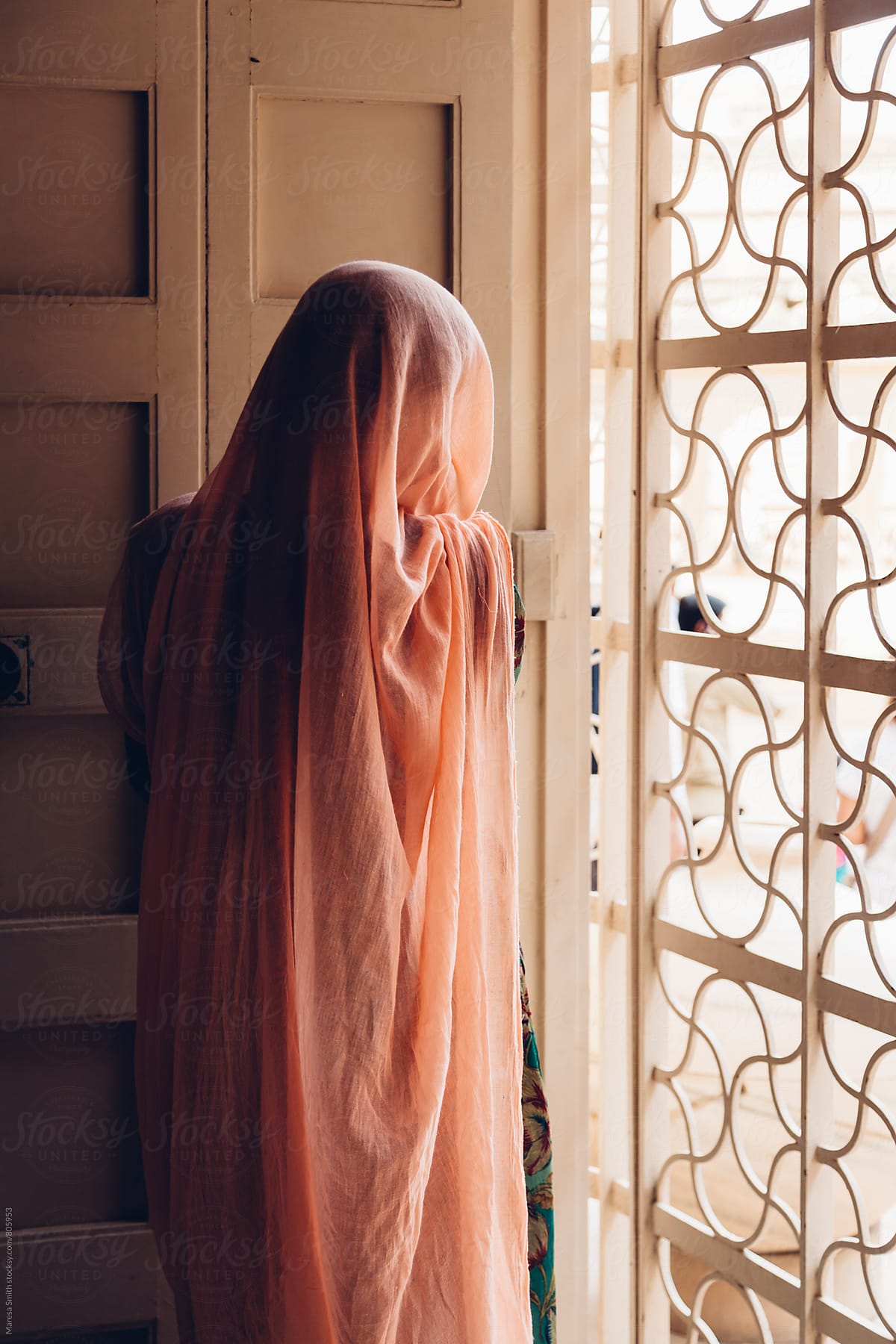 Anonymous women covered in a pale pink sari looking out of a window