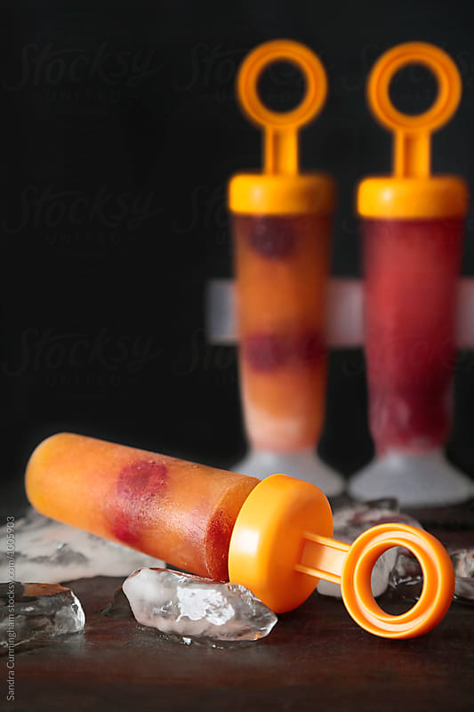 Fresh orange and berry popsicles on table