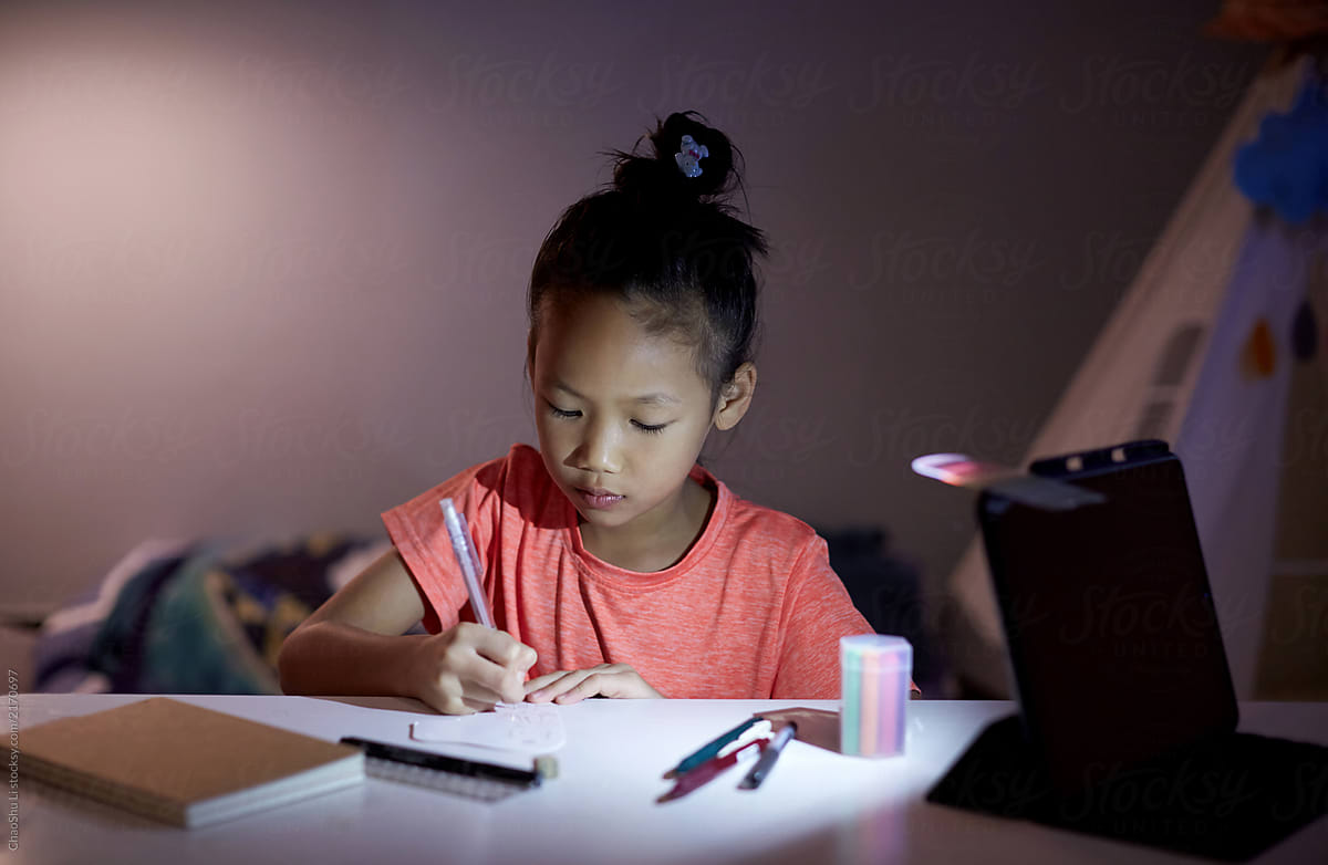 Seriously drawing Asian little girl, in the evening home