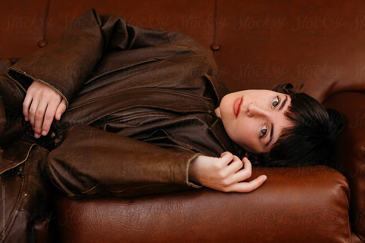 Young stylish dark haired woman lying on brown leather sofa