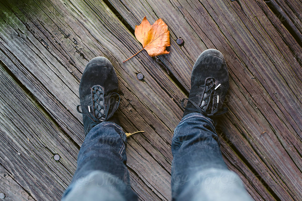 Orange Leaf Between Feet Wearing Sneakers On Boardwalk By Stocksy