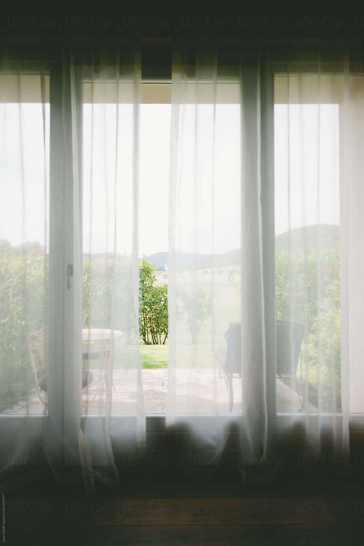 Garden seen from the inside through linen curtains and glass door