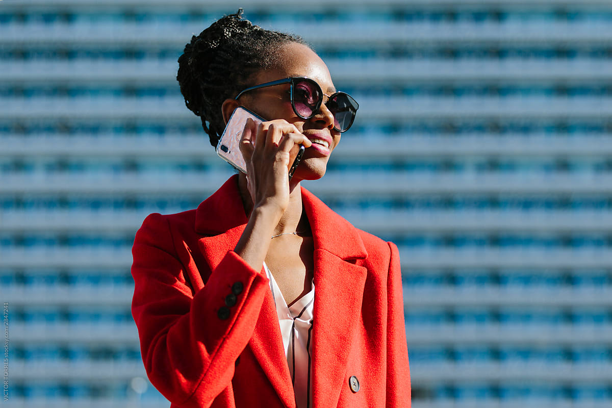 Stylish black businesswoman in red jacket speaking on smartphone