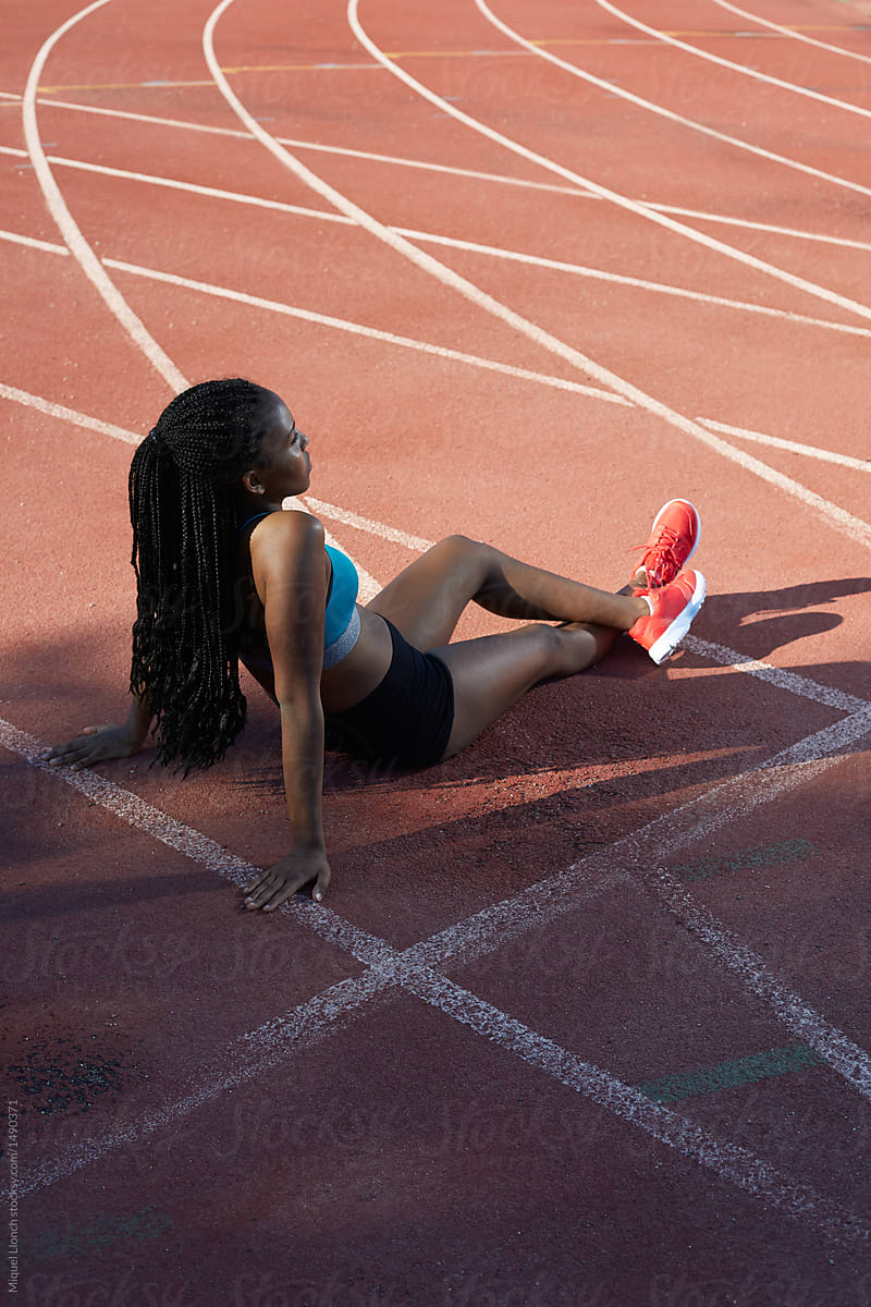 Black athlete sitting on ground of track and field