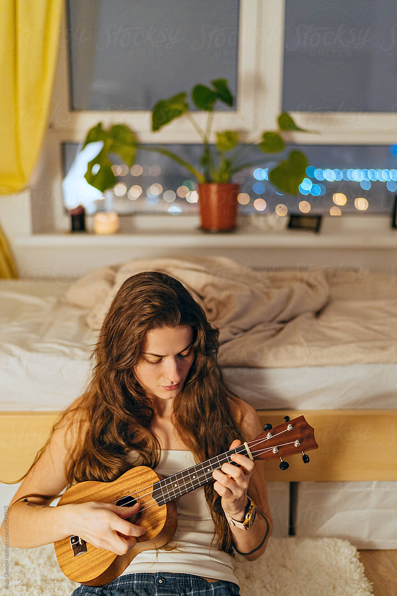 young woman playing ukulele in her room in the evening