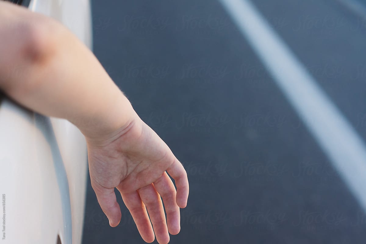 Teenager\'s hand and arm hang out car window on warm day