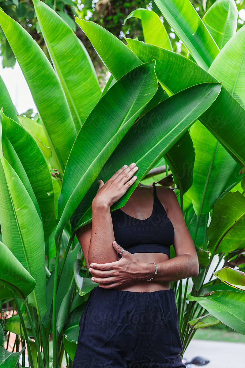 Anonymous slim woman hiding behind exotic plant