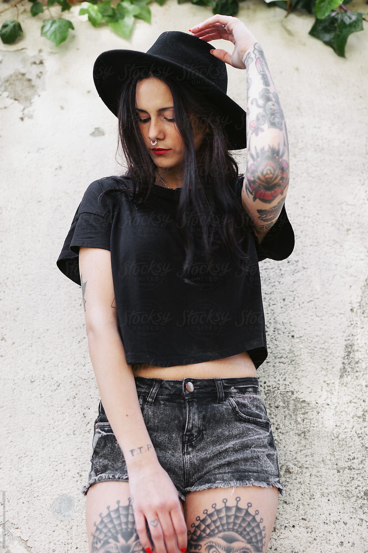 Young alternative woman with tattoos posing in front a wall.