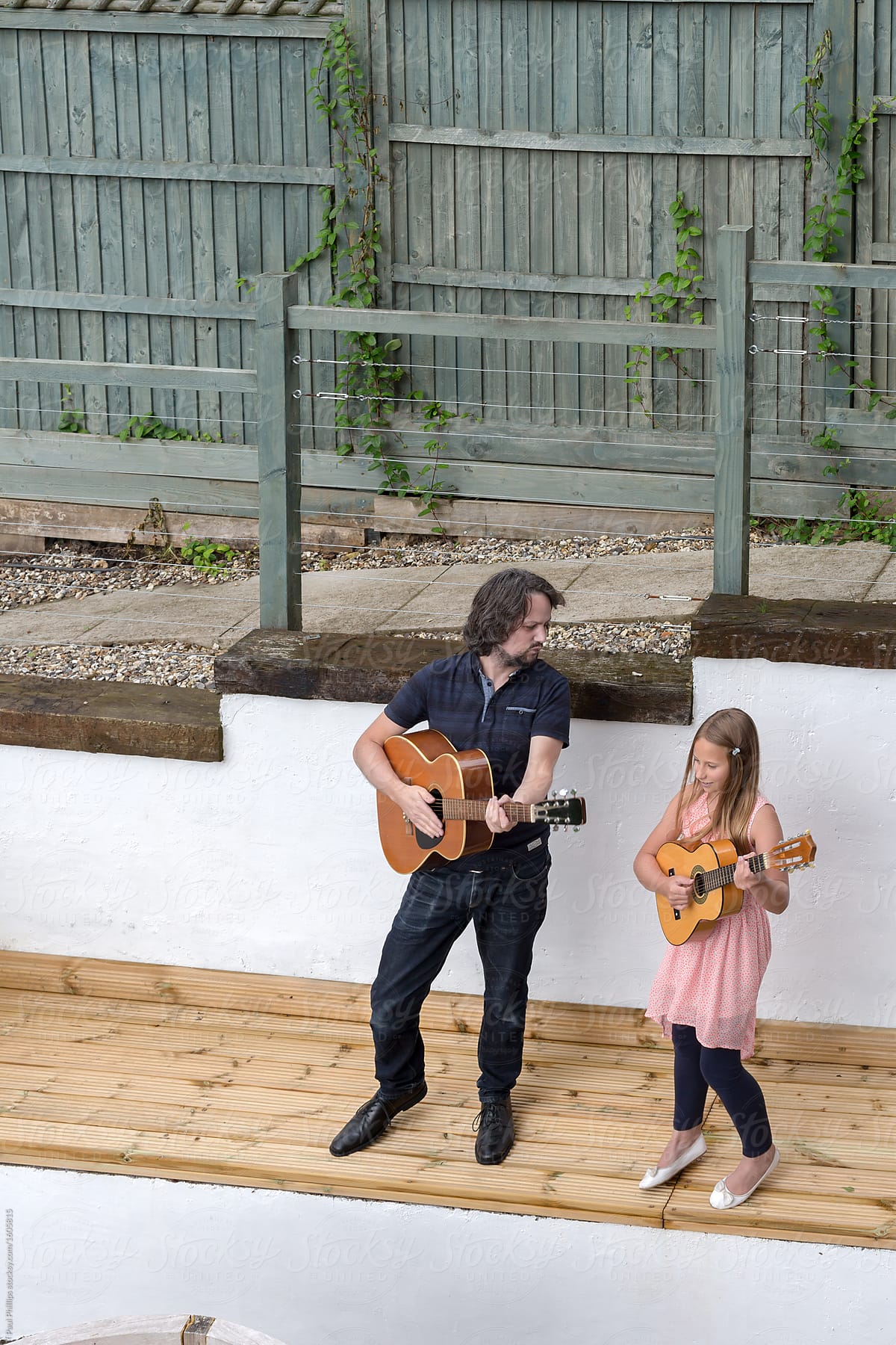 Father and daughter playing guitar on a raised area of their garden patio,