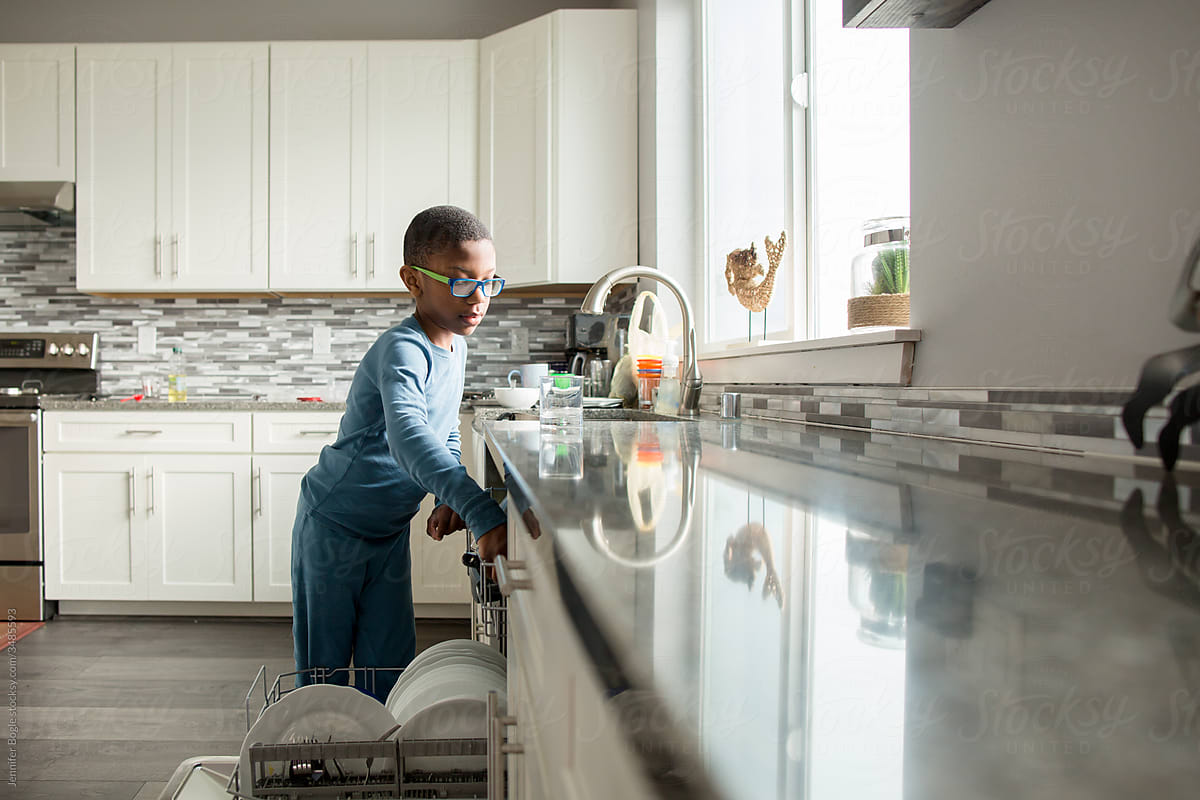 Boy loads dishwasher in bright kitchen