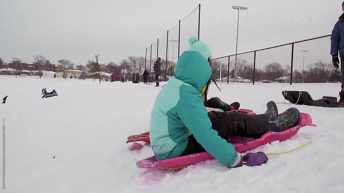 Caucasian And Black Girls Sledding Down A Hill Backwards In Slow Motion By Stocksy Contributor