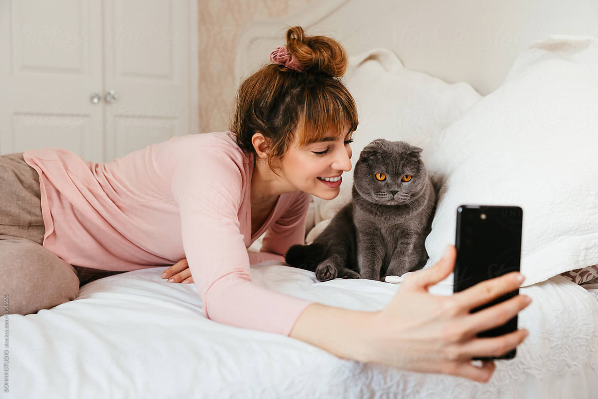 Happy woman taking self shot with cat on bed