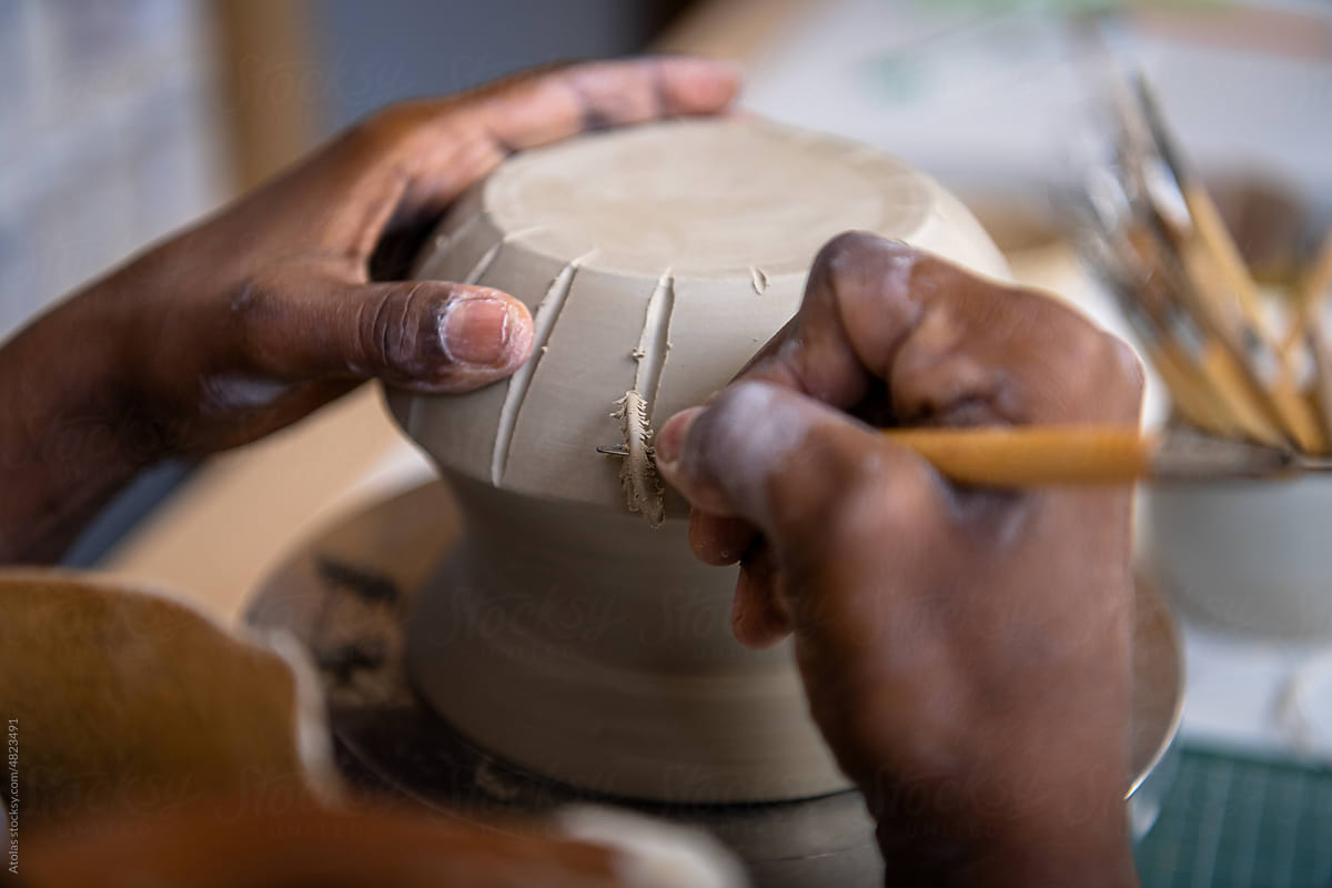 Closeup of a woman's hands working on pottery at her desk