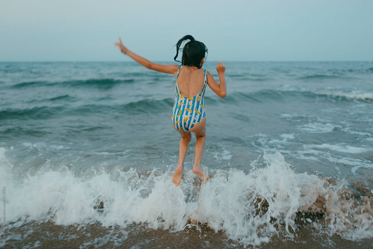 Back view of kid jumping a wave in the sea.