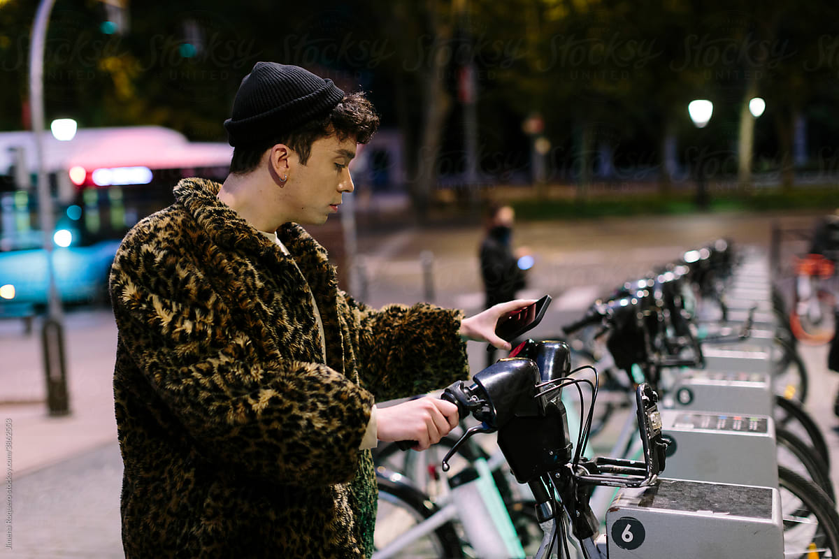 Gen-z non-binary person using his smartphone to unlock a rental city bike