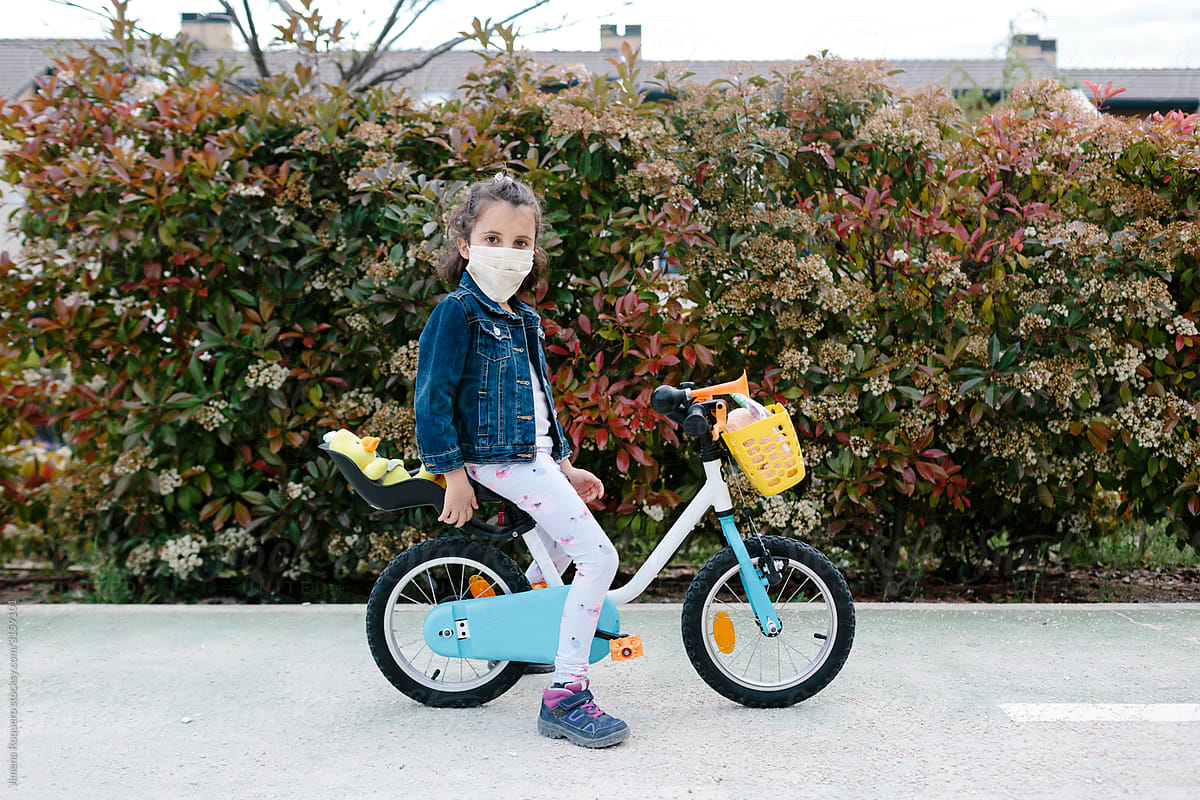 Kid riding her bike with protective face-mask looking at camera