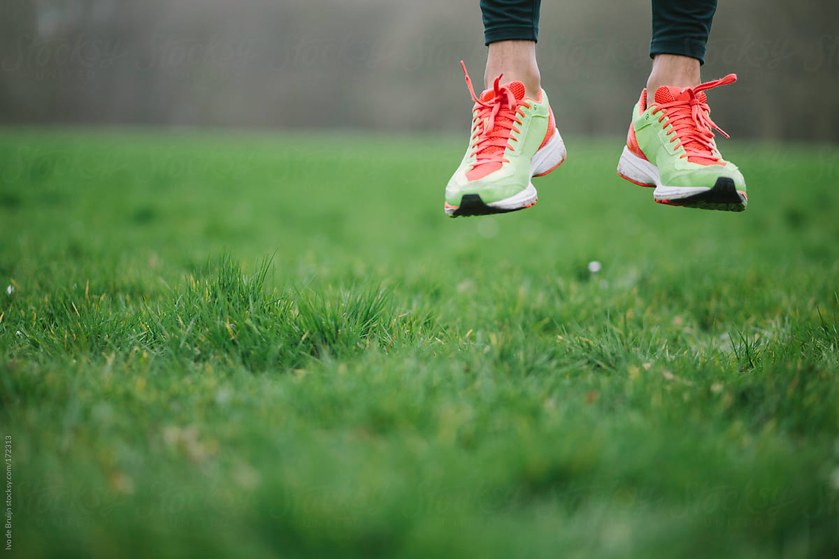 A close up of a runner's shoes jumping off the grass