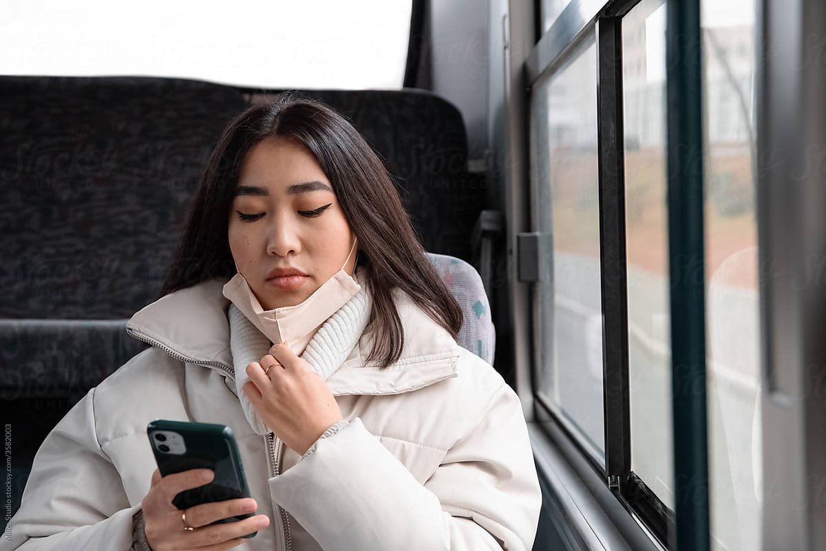 Asian female with mask using cellphone in bus