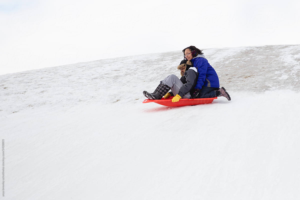 Mother and her teenage daughter tobogganing down a hill