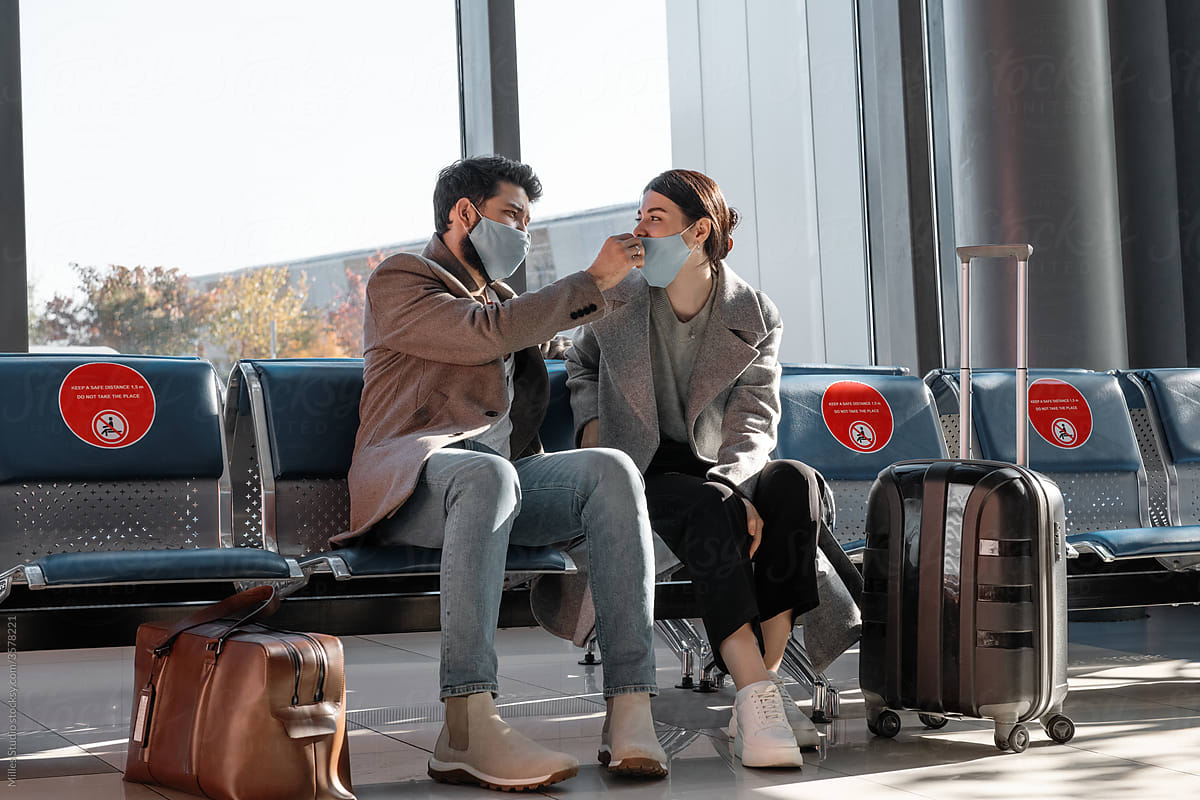 Man adjusting mask on woman in airport waiting room