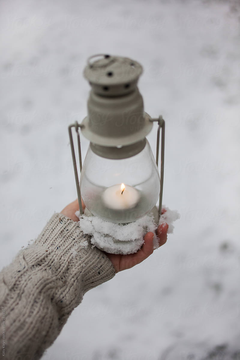 Hand grasping a lit lantern in the snow