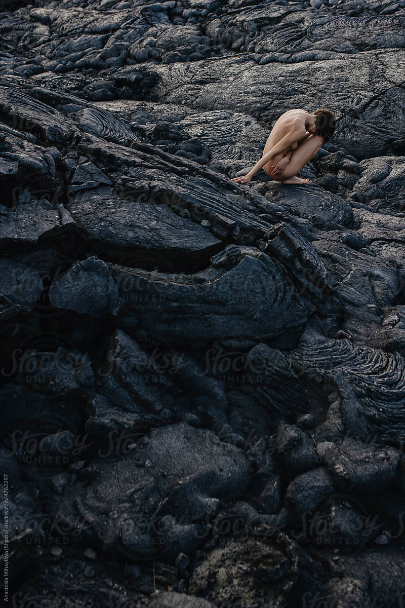 Naked female sitting on black solid lava field in Iceland