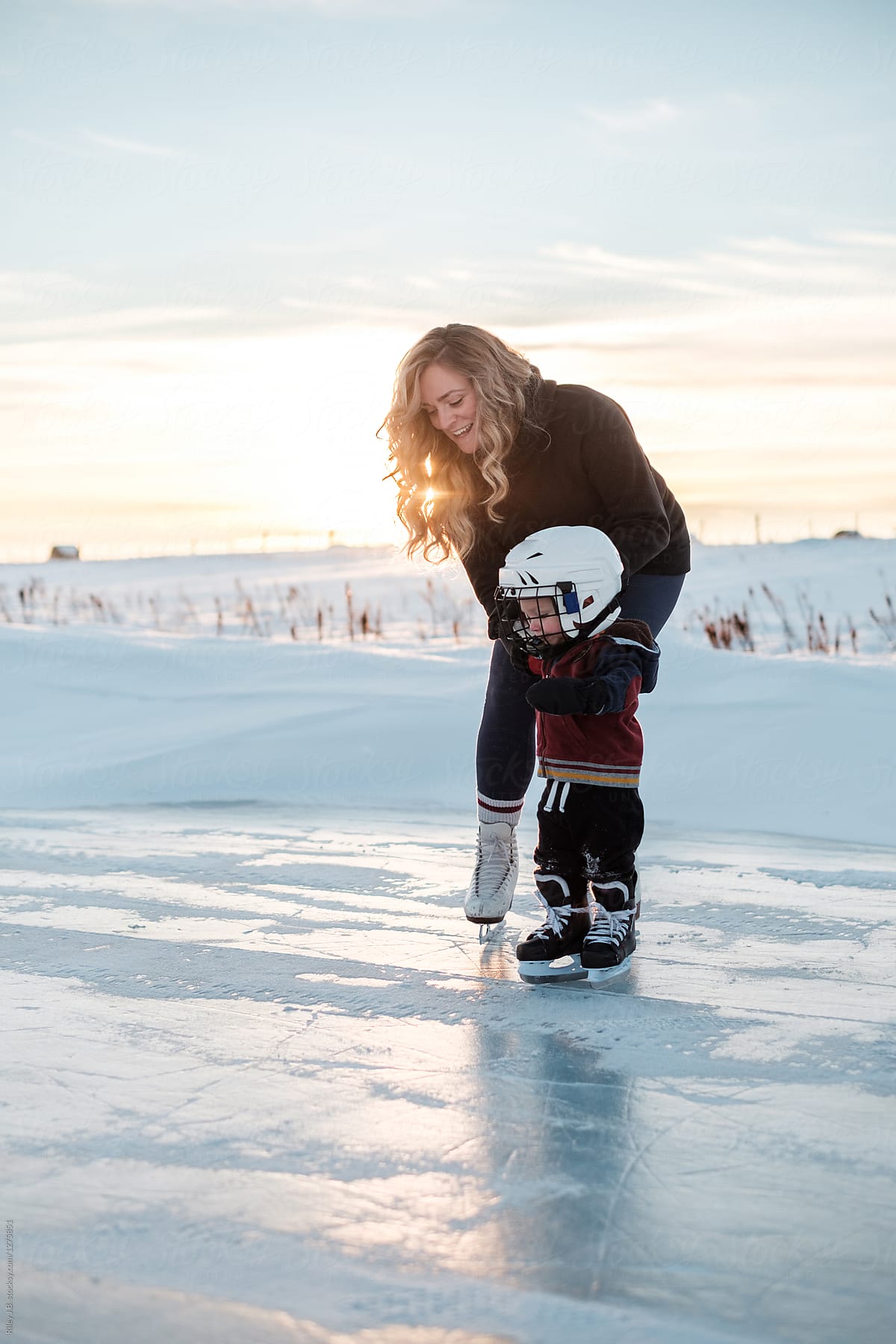A pretty Mother helps her son skate on a frozen pond.