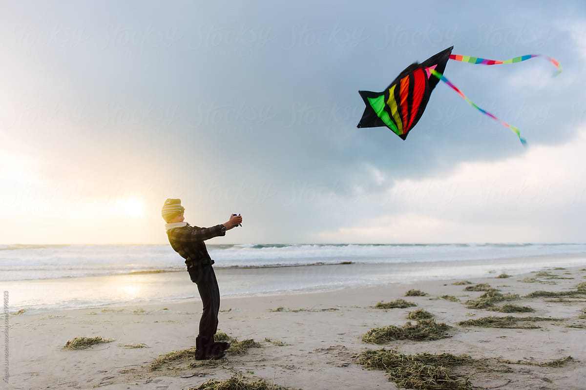 Boy at the beach in winter, flying a kite in stormy weather