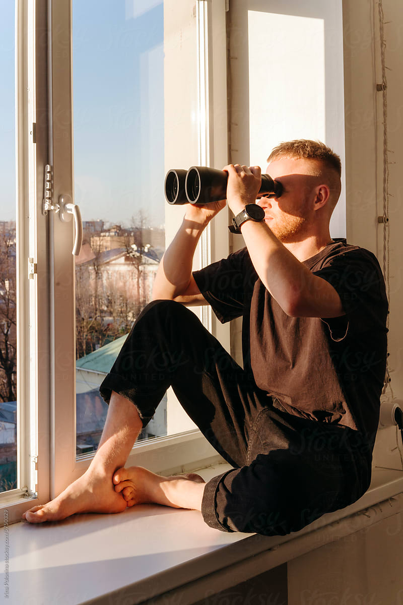 Man looks through binoculars from home.