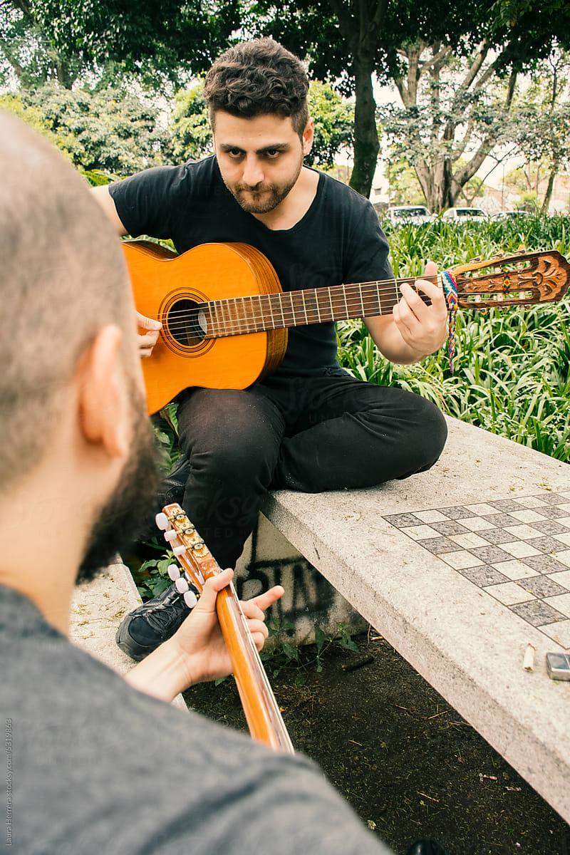 Two men playing guitars on a park bench