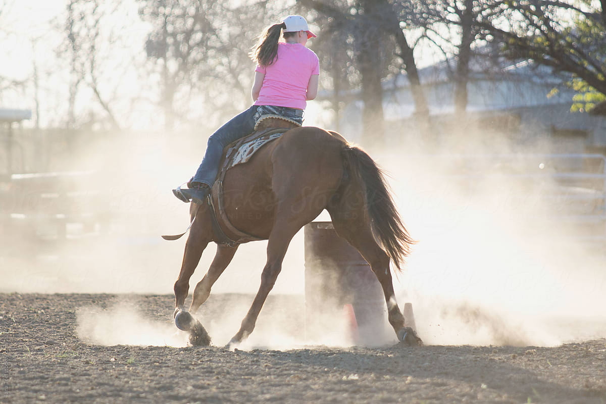 A young woman practices barrel racing with her horse