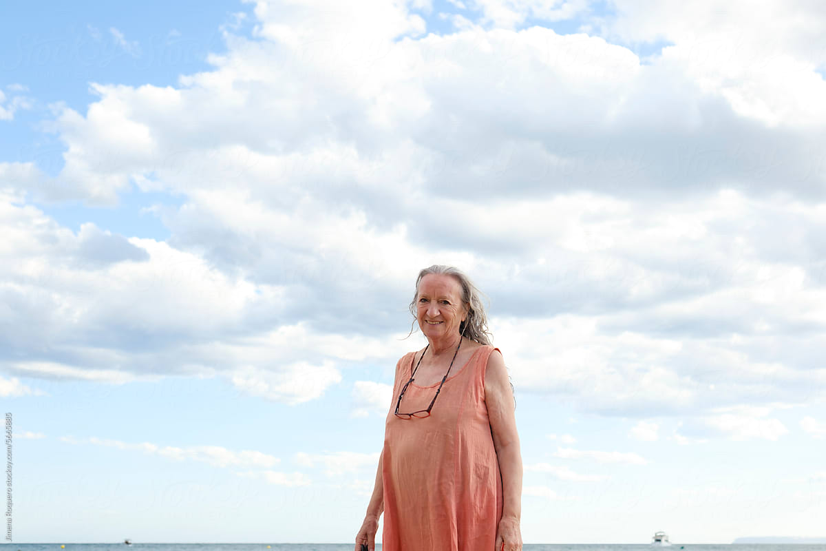 Grey-haired woman in orange dress smiling over blue sky