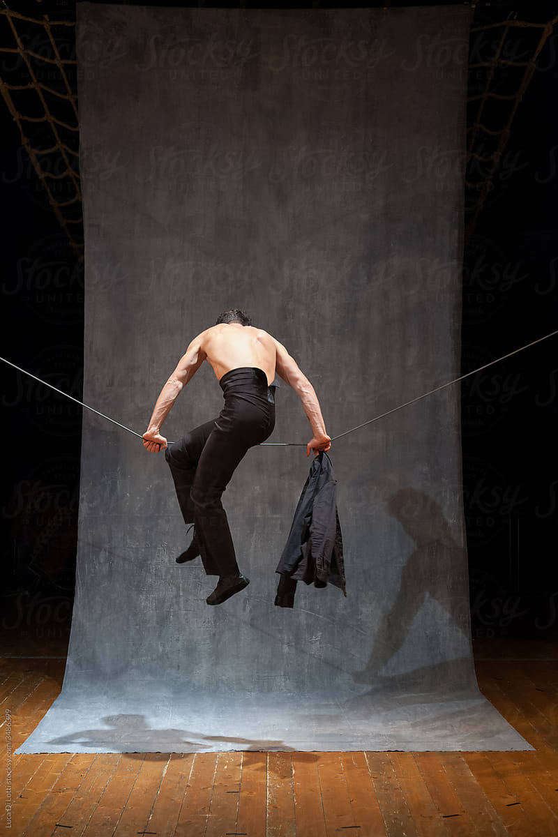 Shirtless performer climbs on a slackwire.