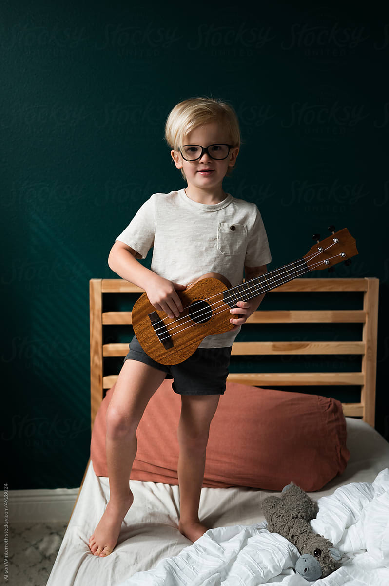 Child playing a guitar as he stands on his bed