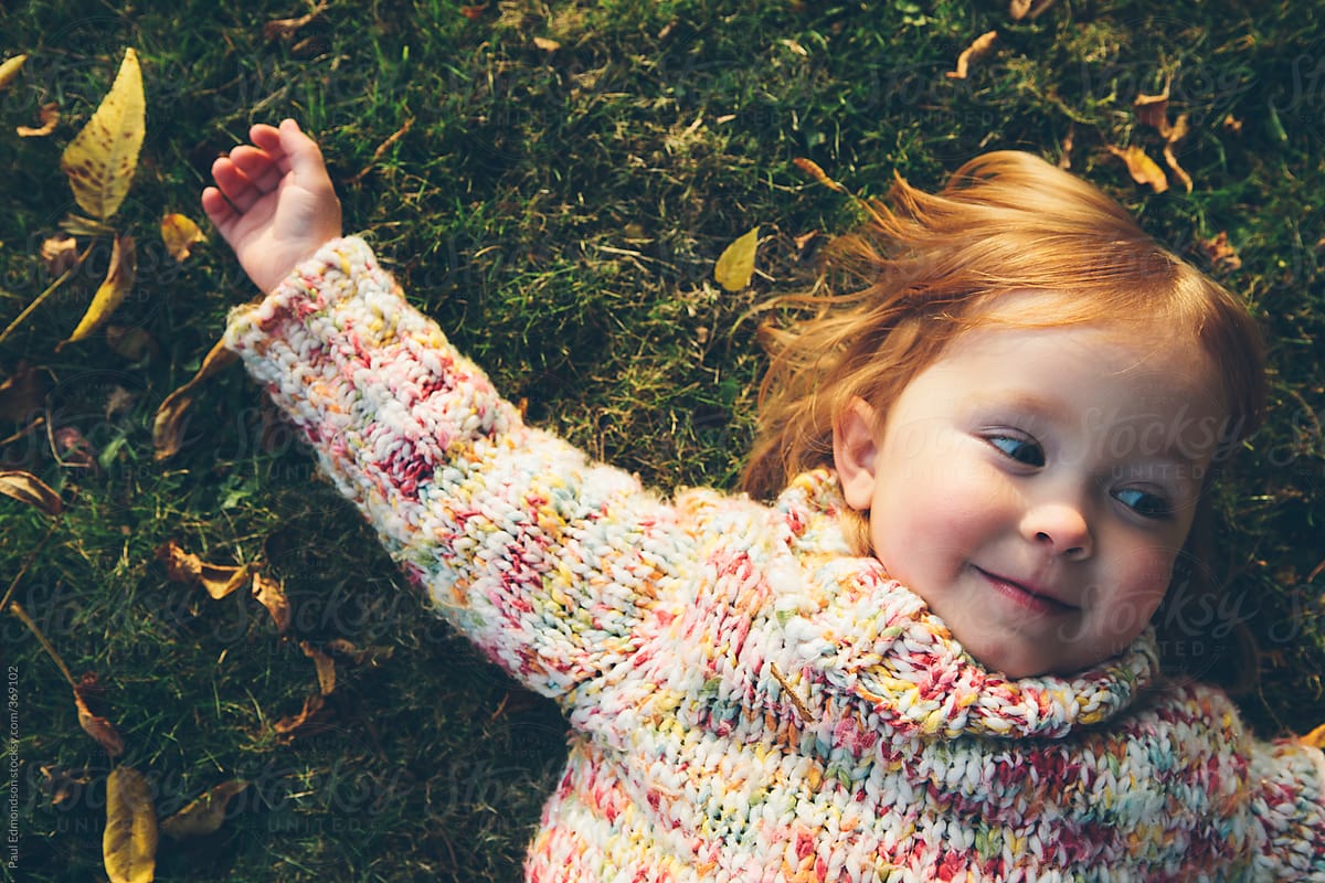 Happy Three Year Old Girl Laying On Grass With Autumn Leaves By Stocksy Contributor Rialto