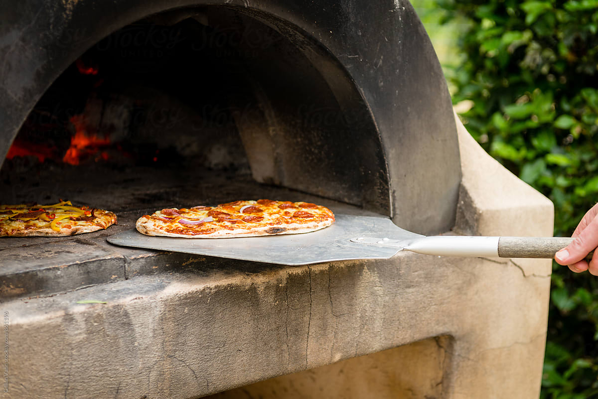 cooking pizza in an outdoor wood fired pizza oven
