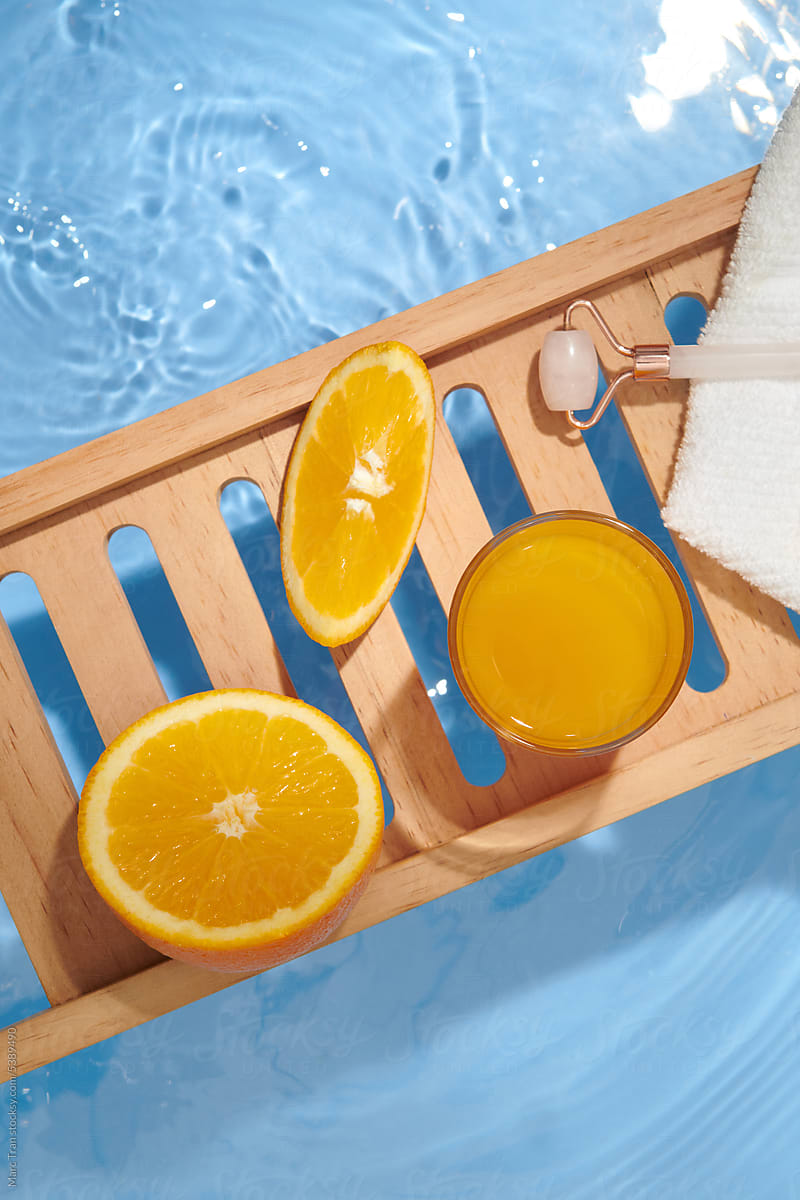 Roller face massager and fresh orange on wooden tray