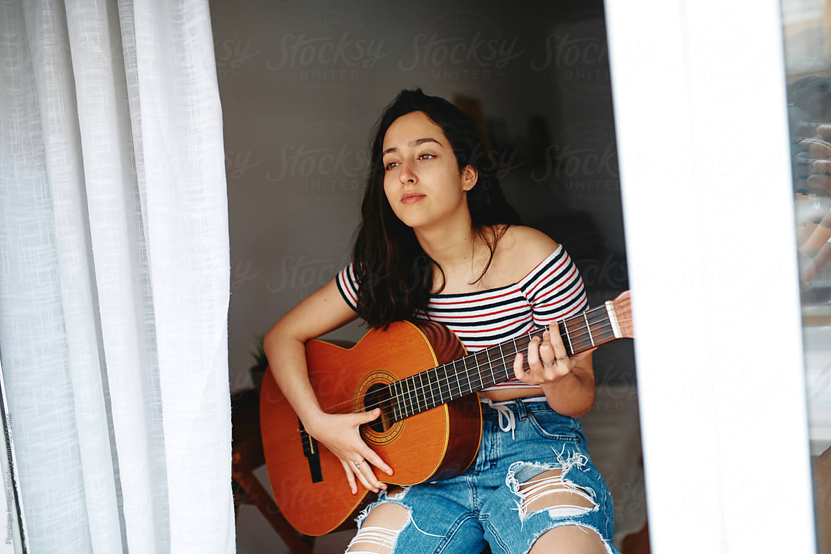 Young woman sitting in her apartment playing guitar