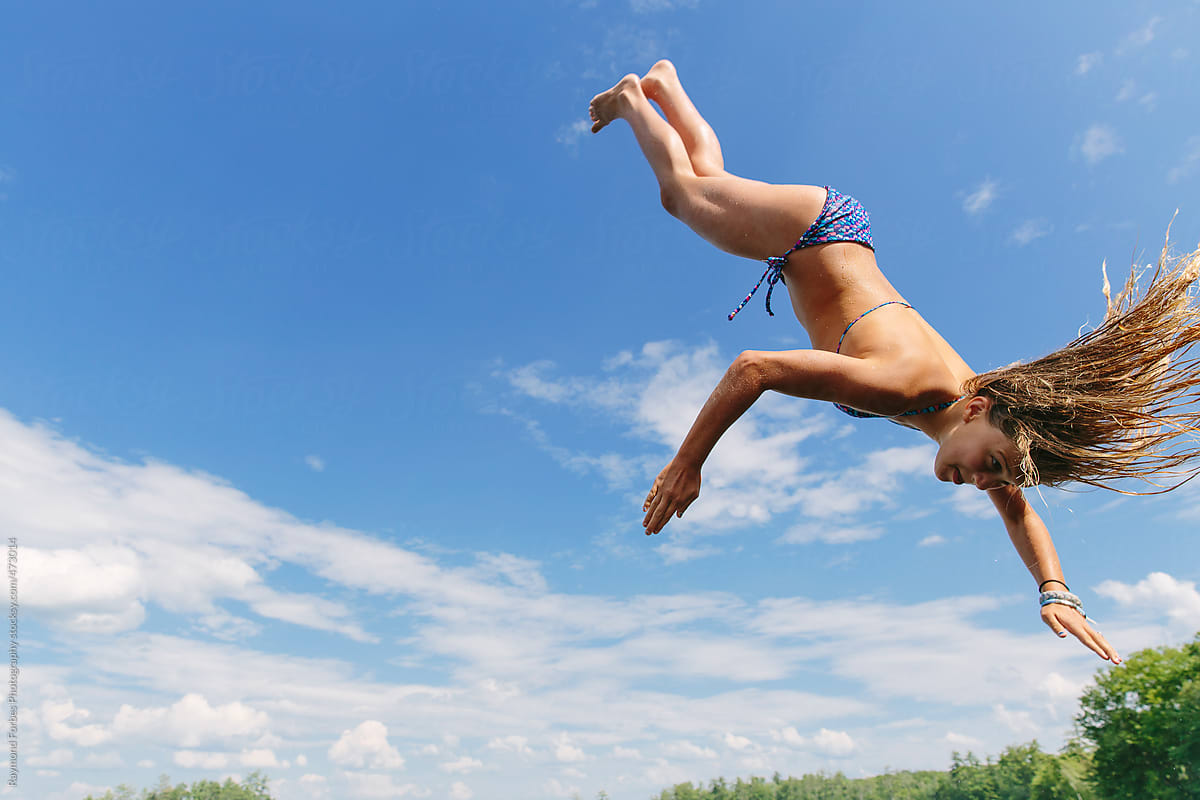 Young girl jumping off the dock into the lake doing flip