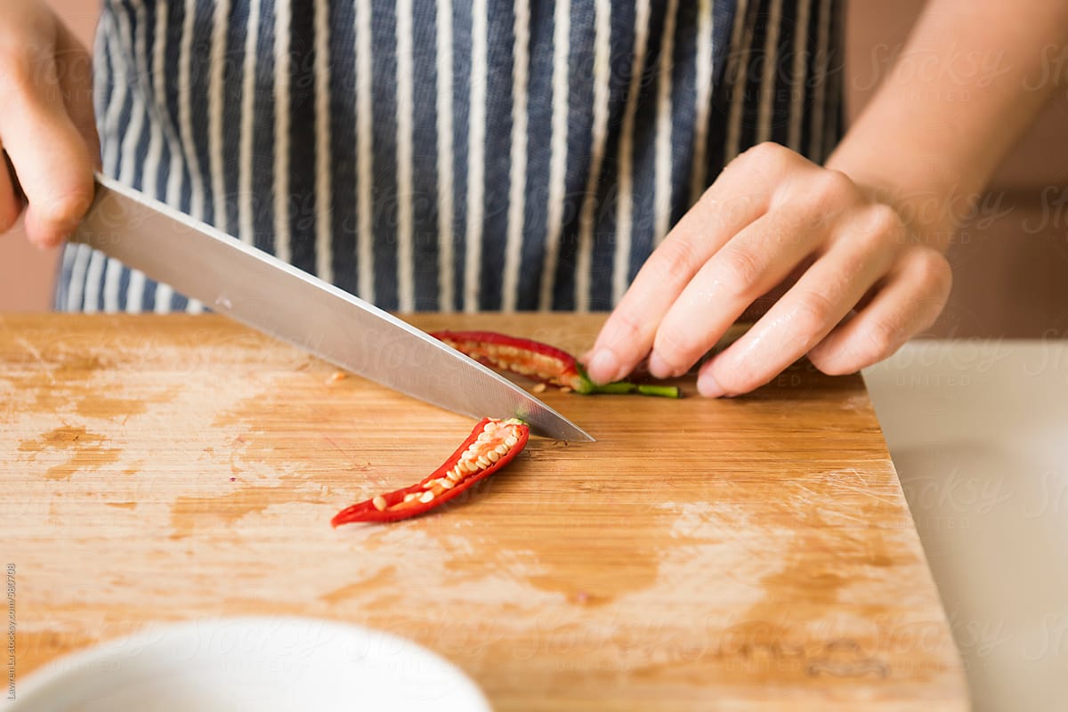Female hands deseeding red chili pepper in kitchen background.