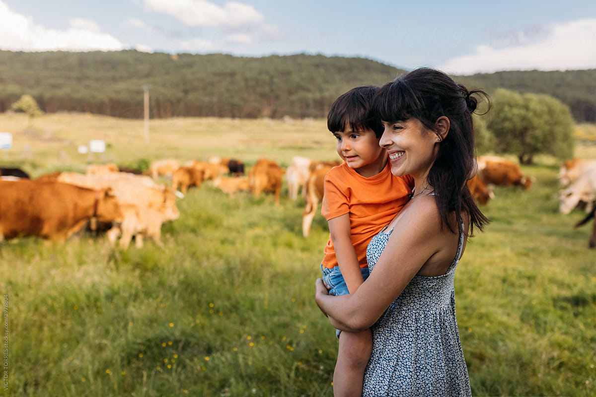 Cheerful mother with kid observing cows in countryside