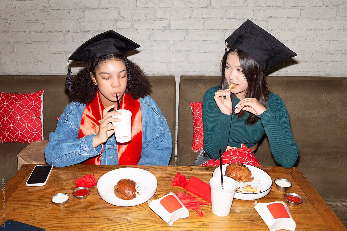 Diverse girlfriends enjoying junk food after graduation