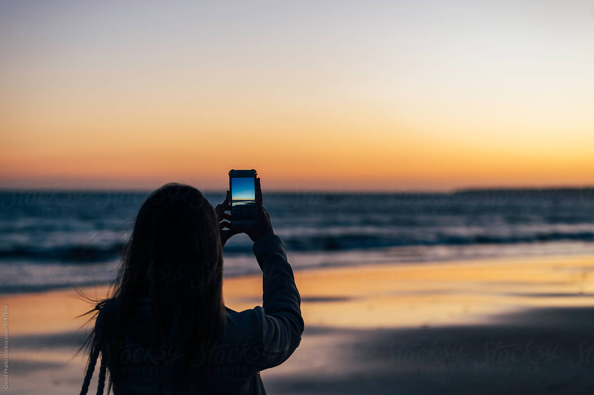 Traveling woman taking photo of sunset over sea