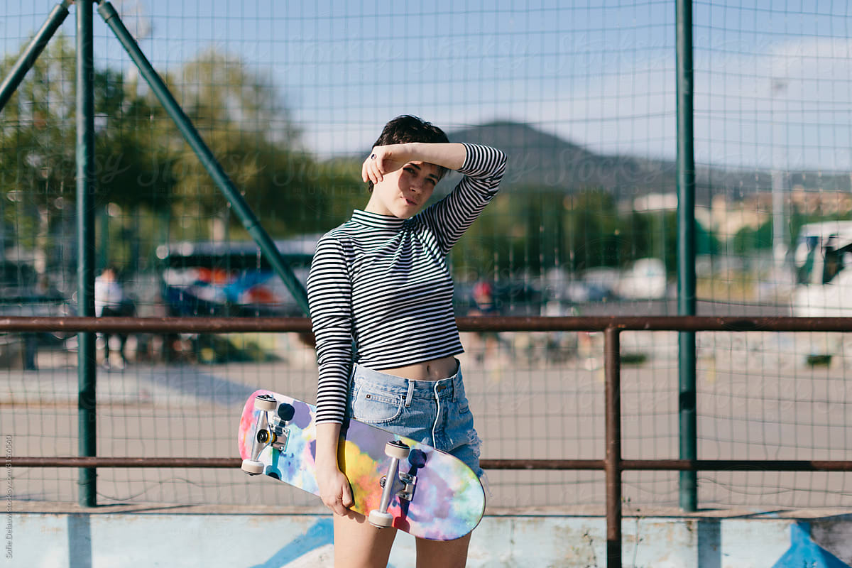 Charismatic young woman with skateboard in park