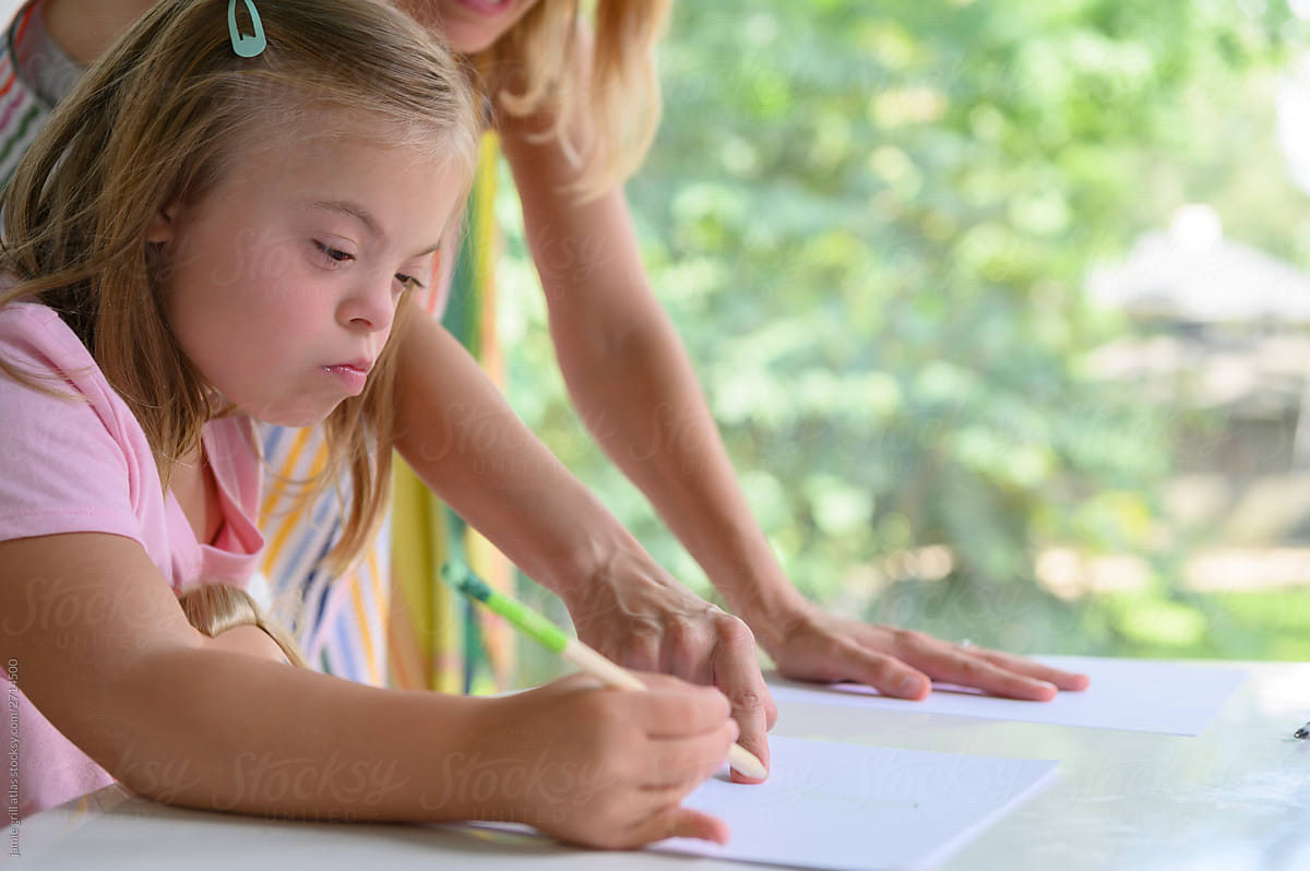 Little girl with down syndrome writing while teacher points