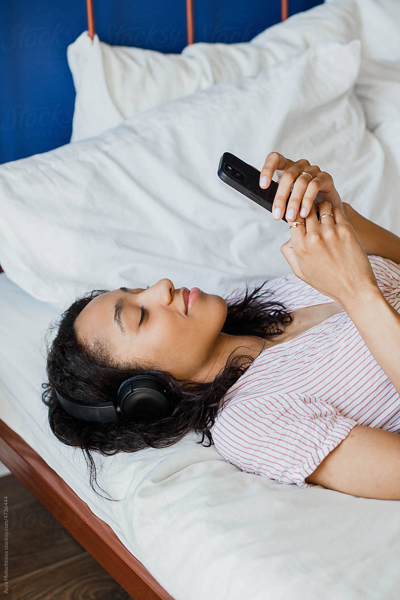 Young woman lying on the bed with headphones and smartphone
