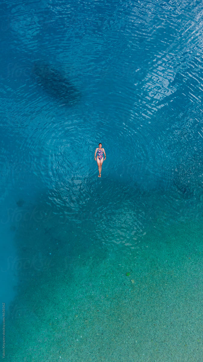 young woman meditating in turquoise sea water, drone overhead