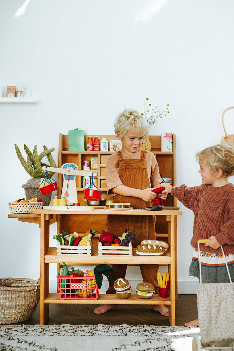 Siblings playing in a wooden play grocery store