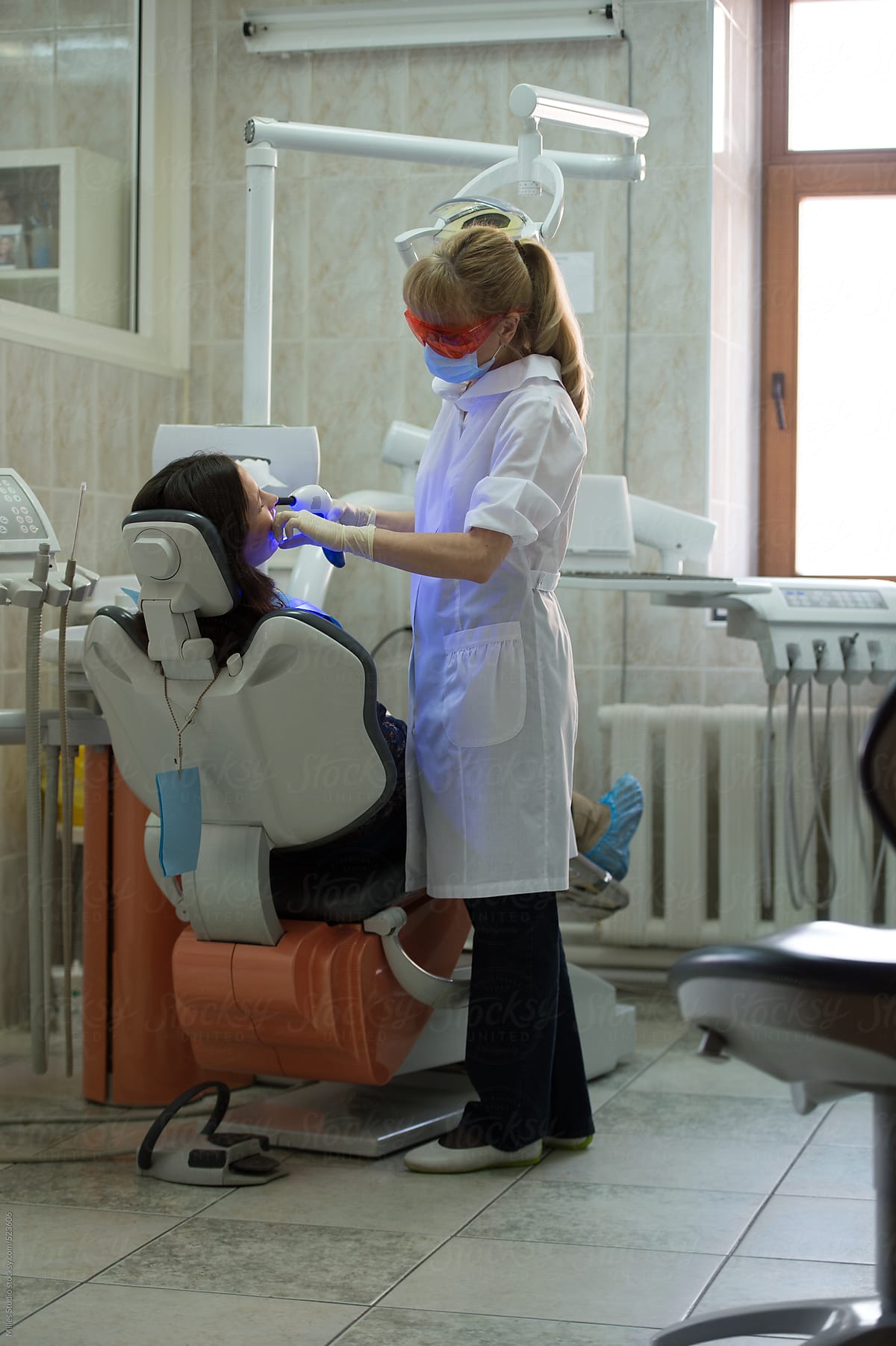 Dentist using ultraviolet curing light equipment to cure patient