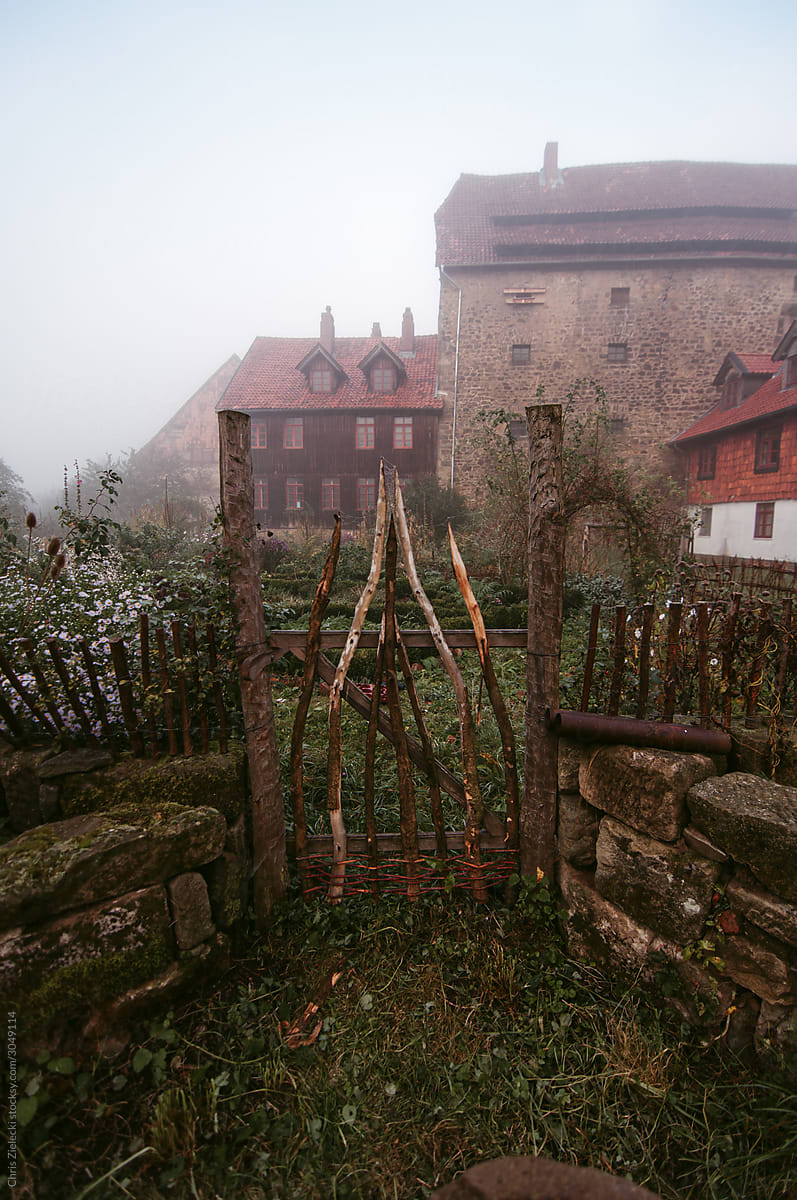 Mystical scenery of abandoned yard with rusty fence against old brick building among fog